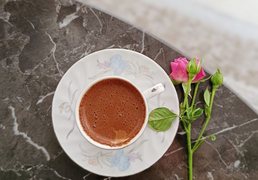 Cană de cafea aburindă pe masă, lângă o fereastră cu lumină de dimineață